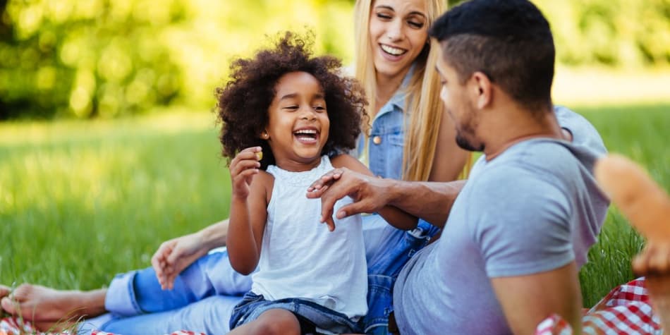 Parents laughing with their child,
    laying on a picnic blanket.