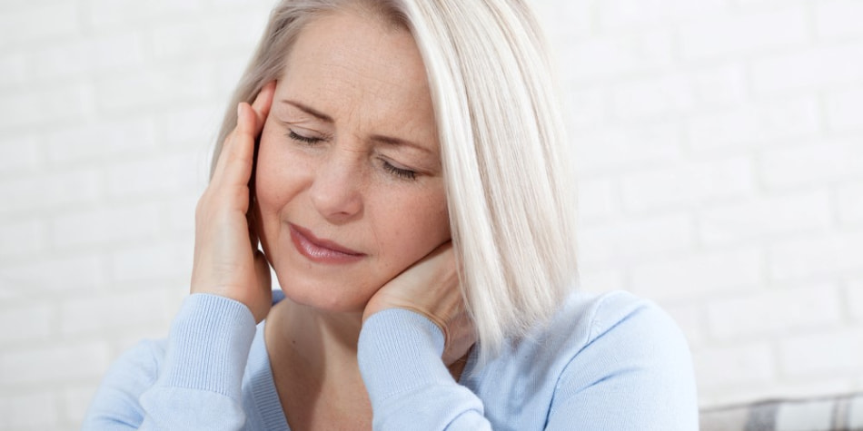 A woman with gray hair holds her neck and ear in pain.