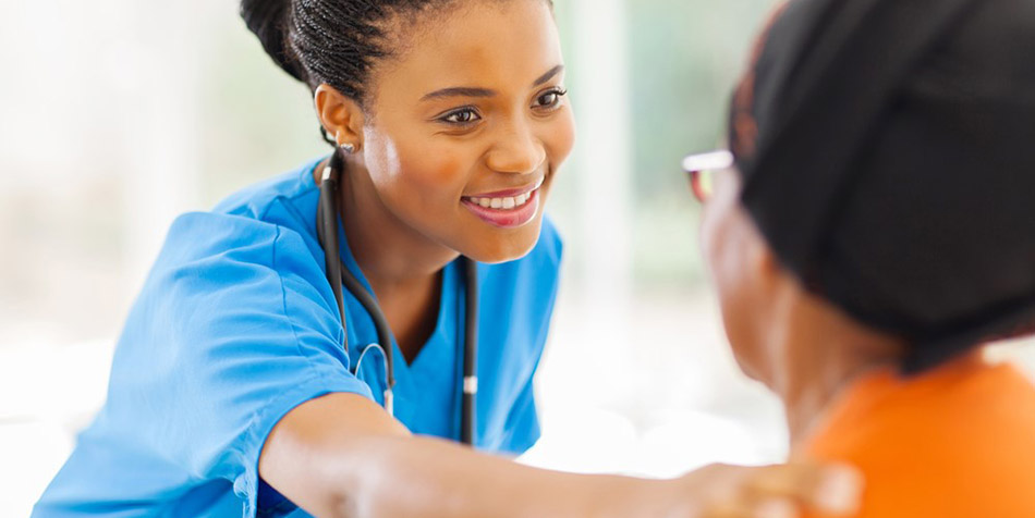 A smiling female doctor in scrubs puts her hand on a female patient's shoulder.