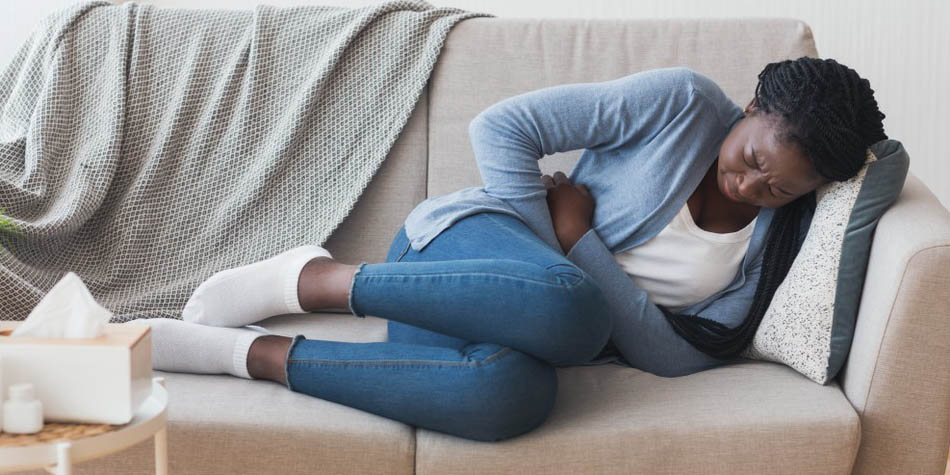 A woman with stomach pain lies on a couch with her hand on her abdomen.