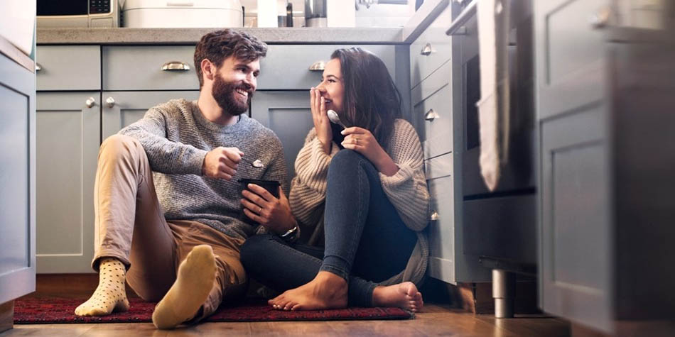 A couple shares a dessert on the kitchen floor.